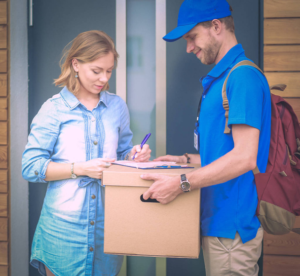 Repartidor sonriente con uniforme azul que entrega la caja de paquetes al destinatario: concepto de servicio de mensajería. Repartidor sonriente en uniforme azul - Foto, Imagen