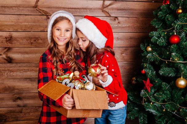 Merry Christmas and Happy Holidays. Cute little sisters decorate the tree at home. - 写真・画像
