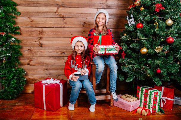 Feliz Navidad y Felices Fiestas. Dos niñas lindo niño con regalo cajas de regalo cerca del árbol de interior
 - Foto, imagen