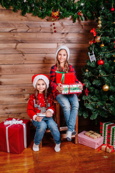 Buon Natale e Buone feste. Due simpatiche bambine con scatole regalo vicino all'albero al coperto
 - Foto, immagini