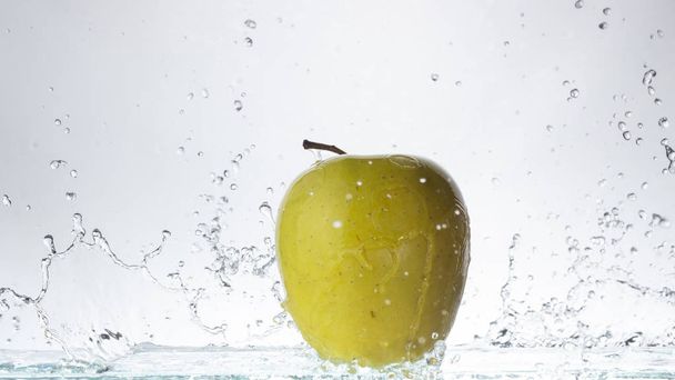Manzana verde sobre un fondo claro y salpicaduras de agua de cerca
 - Foto, imagen