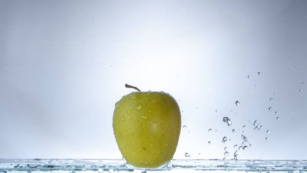 Green apple on a light background and splashing water close up - Fotografie, Obrázek