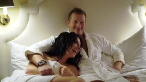 Young sexy couple at night laying in bedroom in white bathrobes or towel and hugging. - Video
