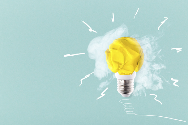 crumpled yellow paper light bulb on a blue background with smoke, concept idea - Photo, Image