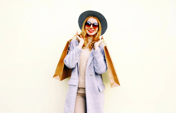 Happy young smiling woman with shopping bags in pink coat, round hat on wall background - Foto, afbeelding
