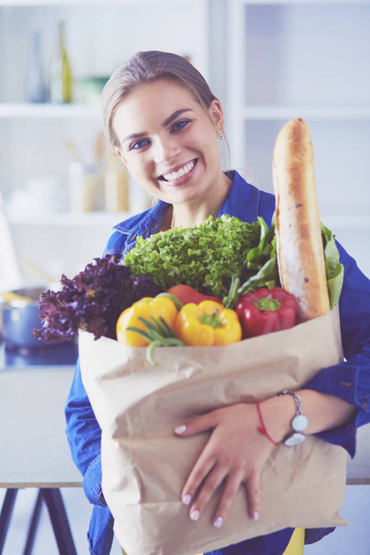 Young woman holding grocery shopping bag with vegetables .Standing in the kitchen - Fotoğraf, Görsel