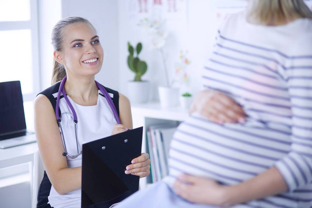 Jovem médica com estetoscópio e tablet falando com mulher grávida no hospital. - Foto, Imagem