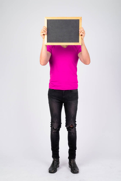 Full body shot of young man showing blackboard and covering face - Fotoğraf, Görsel