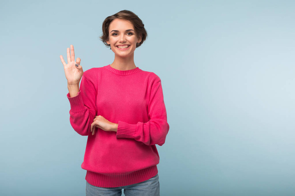 Mladá atraktivní žena s krátkými vlasy tmavě růžový svetr zobrazeno třemi prsty gesto šťastně pohledu kamery nad modrým pozadím - Fotografie, Obrázek