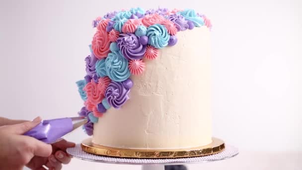 Baker piping pastel color buttercream rosettes on a white cake to make a unicorn cake. - Footage, Video