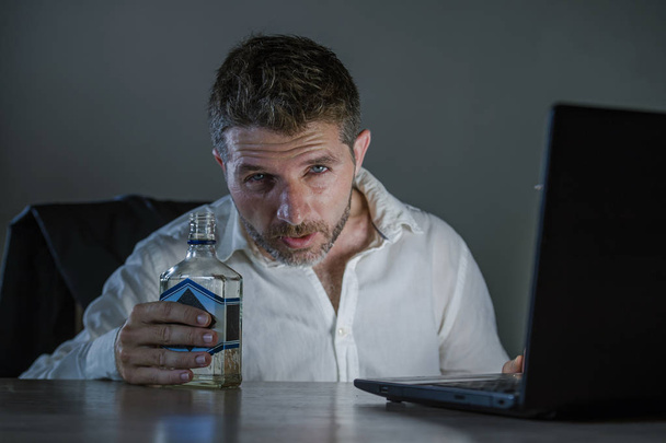 young wasted and depressed alcohol addict  businessman drinking bottle working drunk late night at office laptop computer desk intoxicated suffering depression and alcoholism problem - Valokuva, kuva