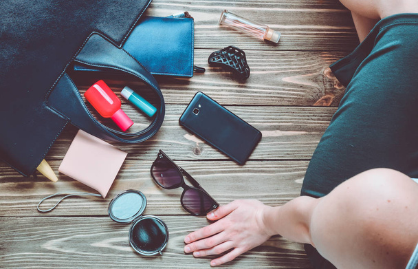 Was ist in der Frauentasche? Modische Accessoires für Frauen auf einem hölzernen Hintergrund. Smartphone, Parfümflasche, Powerbank, Spiegel, Sonnenbrille, Lippenstift. Ansicht von oben. - Foto, Bild