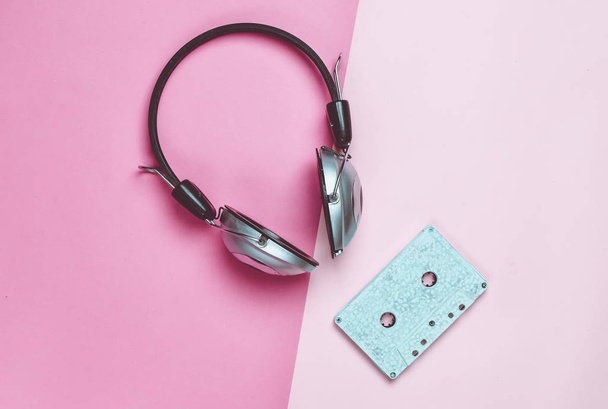 Drahtlose Kopfhörer und Audiokassetten auf buntem Pastellpapier-Hintergrund. minimale kreative Kunst. Musikalische Retro-Vibrationen. Ansicht von oben. - Foto, Bild