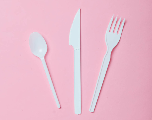 Posate di plastica per picnic su sfondo rosa. Cucchiaio usa e getta, forchetta, coltello. Vista dall'alto, copia spazio
. - Foto, immagini
