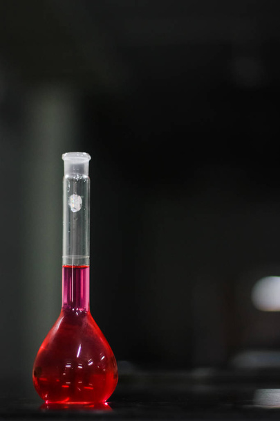 líquido vermelho em um frasco de fundo redondo sobre uma mesa de granito preto em fundo escuro
 - Foto, Imagem