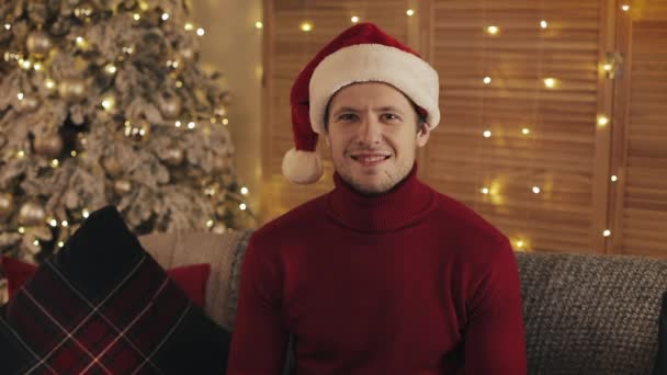 Portrait of Smilling Attractive Man in Santa Hat Looking at the Camera on Christmas Tree Background. Slow motion - Video