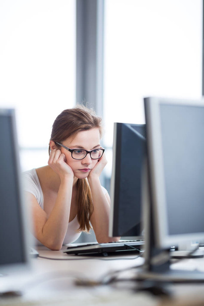 Pretty, female student looking at a desktop computer screen, learning unpleasant news about her exam results. University/office/school concept - Photo, image