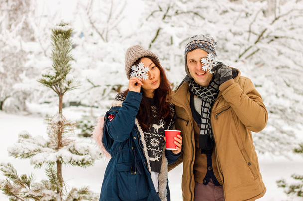 Mooie internationale paar holding sneeuwvlokken en glimlachend in het park in de winter in de sneeuw. - Foto, afbeelding