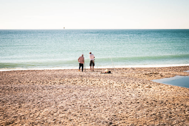 海岸で釣り竿と 2 つの漁師。リアビュー。晴れた夏の日。テキストのための場所. - 写真・画像
