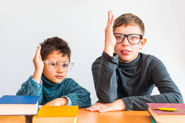 two boys in glasses holding hands up sitting at a Desk - Foto, afbeelding
