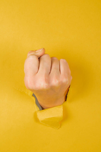 female fist punching through a paper, isolated on a yellow background - Photo, Image