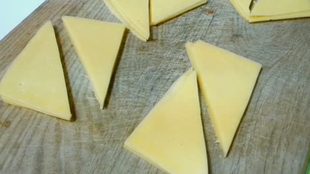 Kaas, gesneden in driehoekige segmenten, ligt op een houten keuken-bord. - Video