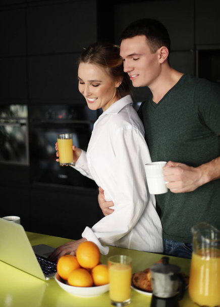 pareja joven en casa tomando café en la cocina y trabajando en el ordenador portátil
 - Foto, Imagen
