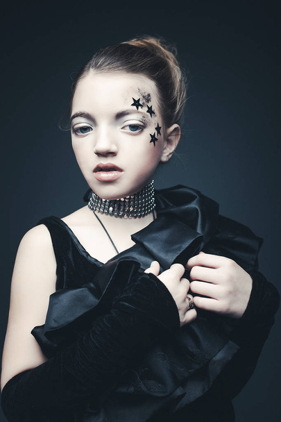 Концепция красоты и моды: маленькая девочка в черном наряде. Креативный макияж
. - Фото, изображение