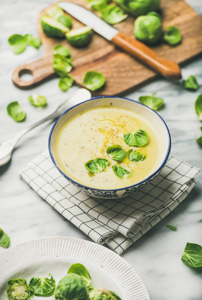 Seasonal brussels sprouts vegetable cream soup in bowl and fresh green brussel sprouts over grey marble background. Vegan, vegetarian, healthy, dieting food concept - Fotoğraf, Görsel