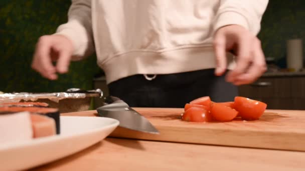 Closeup of girls hands at home kitchen on a wooden cutting board knives small cherry tomatoes with a knife. Home cooking - Footage, Video
