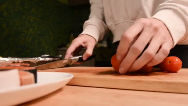 Closeup of girls hands at home kitchen on a wooden cutting board knives small cherry tomatoes with a knife. Home cooking - Materiał filmowy, wideo