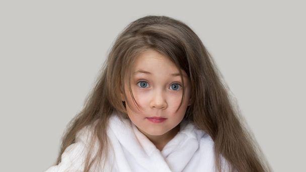 Surprised girl in a white coat. Girl 4-5 years old with long flowing hair in a white bathrobe after a bath. - Photo, Image