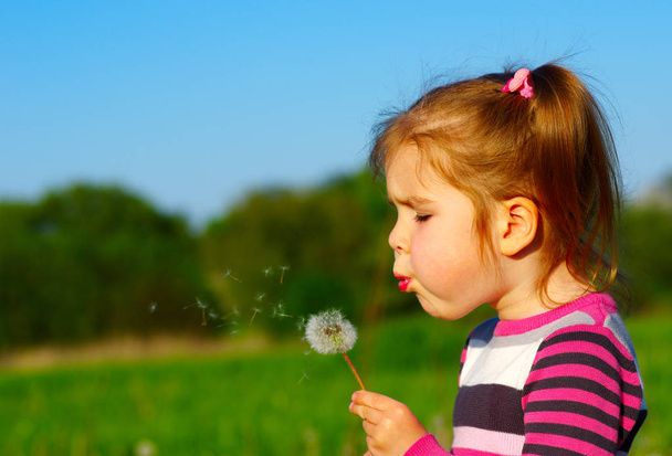 Девушка дует одуванчик на открытом воздухе в весеннем поле
 - Фото, изображение