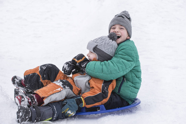 Dva snímky radostné chlapci dolů z kopce na sněhu talířek. Bratrské přátelství. Zimní den. - Fotografie, Obrázek