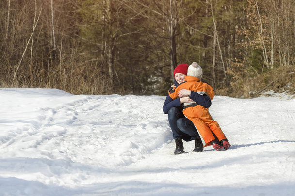 Mutter umarmt den kleinen Sohn vor Kiefernwäldern. Winterlicher Schneetag im Nadelwald - Foto, Bild