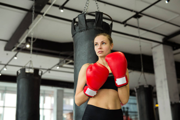beautiful young girl in boxing gloves near the punching bag in the gym in training - Photo, Image