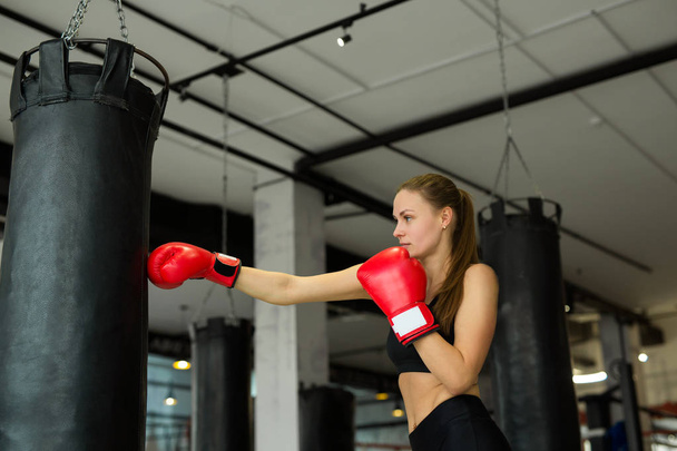 beautiful young girl is engaged in boxing with a punching bag in the gym - Фото, изображение