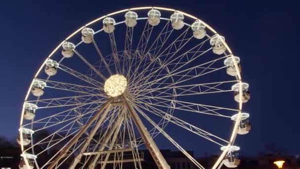 Медленное вращающееся колесо обозрения в вечернем освещении на Рождественской ярмарке на ярмарке, темно-синее небо. Карнавал на колесах обозрения на новогодних распродажах. Забавная поездка на вращающемся панорамном колесе в свете на рынке
 - Кадры, видео