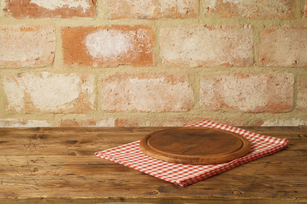 Wooden pizza tray on table with tablecloth over brick wall background - Foto, afbeelding