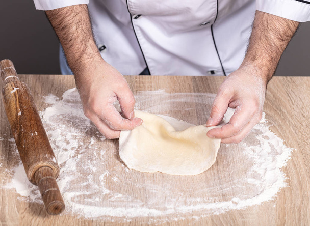 male cook kneads dough on the table, hands close-up - Foto, Imagem