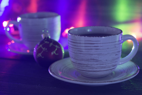Cup of hot coffe on wooden background. Blur christmas lights on wooden planks, low depth of focus. - Photo, Image