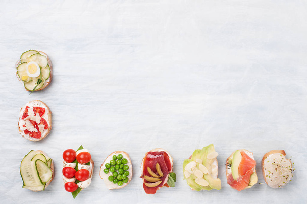 Une variété de canapés avec des légumes, des champignons, du saumon, du jambon et des légumes verts sur le papier parchemin.
. - Photo, image