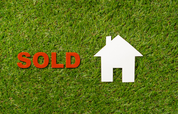 Conceptual picture of paper house and word Sold on green grass field top view and copy space in Property investment business Real estate selling and buying a home mortgage and loan banking concept. - Photo, Image