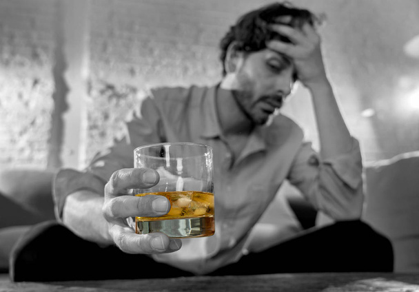 Drunk young man drinking alcohol at home felling lonely depressed and sick holding a glass of whiskey image in white and black and drink in color in Alcohol Addiction Social drug and Abuse concept. - Foto, Bild