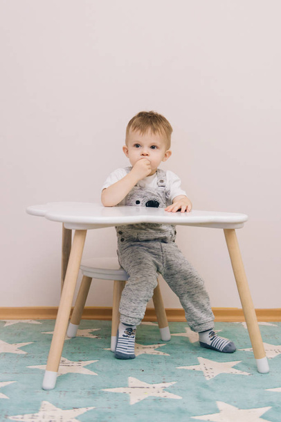 Söpö vauva istuu pöydässä ja syö lastenhuoneessa kirkkaita värejä
. - Valokuva, kuva