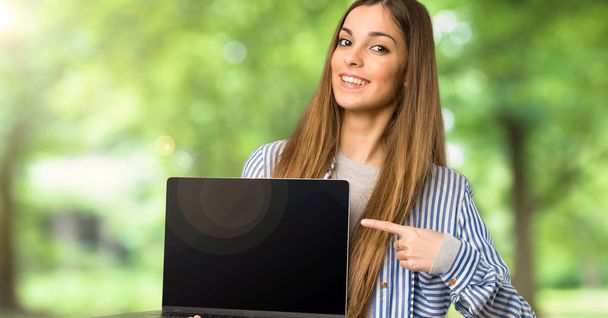 Young girl with striped shirt showing a laptop at outdoors - Photo, image