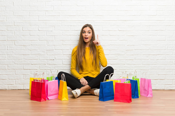 Chica joven con un montón de bolsas de compras pensando en una idea apuntando con el dedo hacia arriba
 - Foto, Imagen