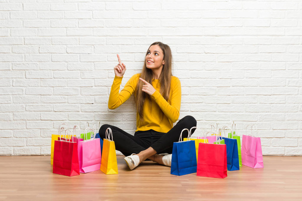 Young girl with lot of shopping bags pointing with the index finger and looking up - Photo, Image