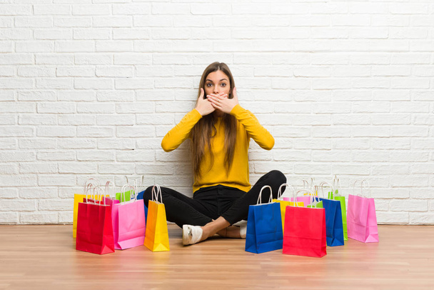 Young girl with lot of shopping bags covering mouth with hands for saying something inappropriate - Photo, Image