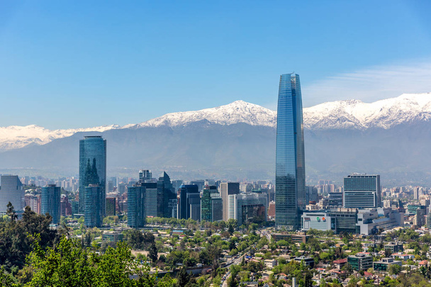 Abundância de edifícios de negócios em Santiago del Chile com árvores em primeiro plano e as montanhas dos Andes em segundo plano
 - Foto, Imagem